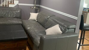 Una sala de estar con un sofá seccional gris, una mesa de centro de madera y un sillón azul.