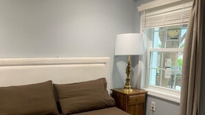 Una cama bien hecha con cabecera, lámpara de noche y ventana con cortinas.