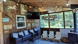 A rustic interior with wooden walls, a sofa, chairs, a TV, and a sign reading "Little Hook Saloon". - Coastal Escape: Cottage Complex (Brackley Beach)