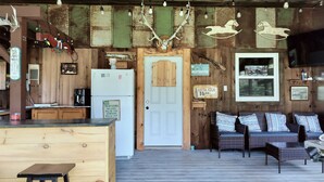 A rustic cabin interior with a wooden dining area, a refrigerator, a sofa set, and a mounted television. - Coastal Escape: Cottage Complex (Brackley Beach)