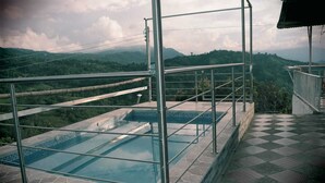 A rooftop infinity pool with a glass barrier, surrounded by stone tiles, overlooking a mountainous landscape. - Finca Recreativa los Altos Giraldos (Arbeláez)