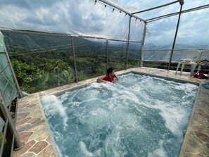 Un bain à remous où se trouve un enfant, entouré d’une enceinte de verre offrant une vue sur un paysage montagneux.