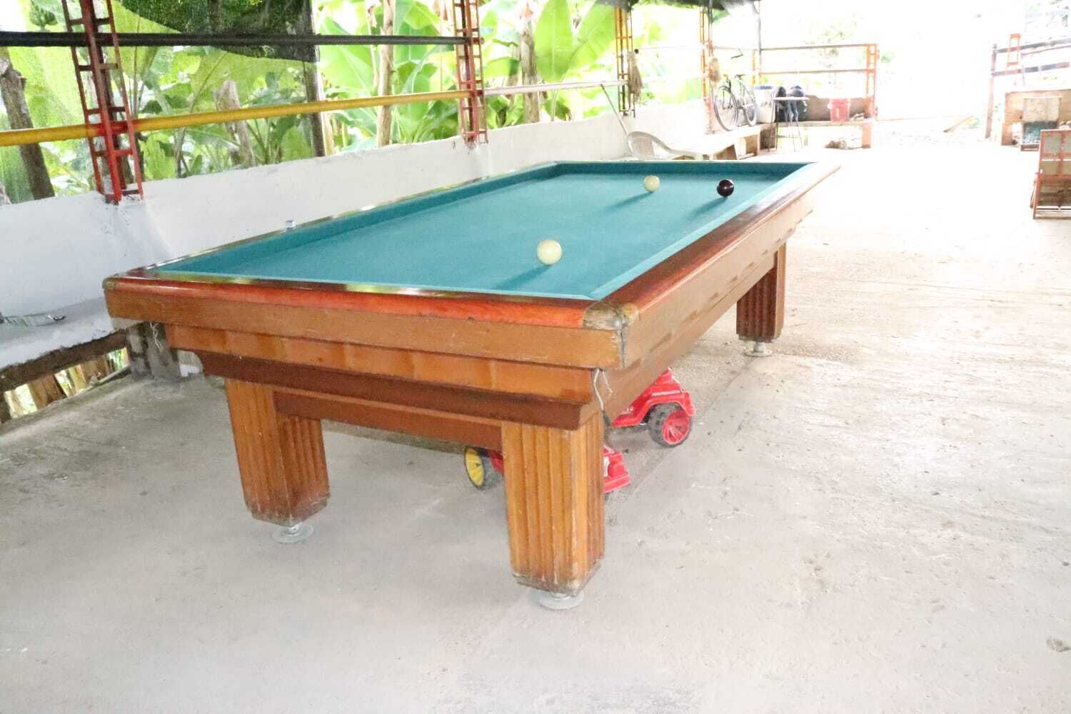 A pool table with a green felt surface, wooden legs, and a red bumper.