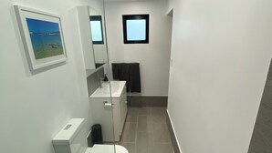 A modern bathroom with a toilet, sink, and mirror. There is a picture on the wall and a small window. - Mindarie Beachside Studio in the coastal suburb of Mindarie, close to the Marina (Mindarie)