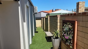 A narrow backyard with artificial grass, a wooden bench, and potted plants. - Mindarie Beachside Studio in the coastal suburb of Mindarie, close to the Marina (Mindarie)