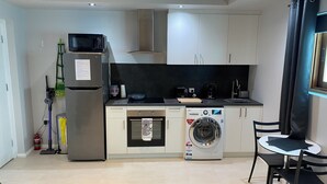 A compact kitchen with a microwave, oven, washing machine, and a small dining area with a table and chairs. - Mindarie Beachside Studio in the coastal suburb of Mindarie, close to the Marina (Mindarie)