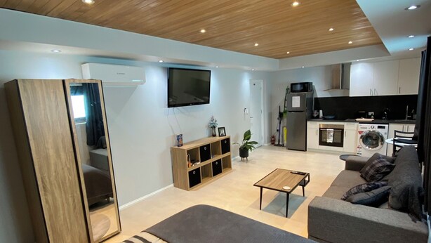 A modern living space with a wooden ceiling, a large bed, a sofa, a TV, and a kitchen area. - Mindarie Beachside Studio in the coastal suburb of Mindarie, close to the Marina (Mindarie)