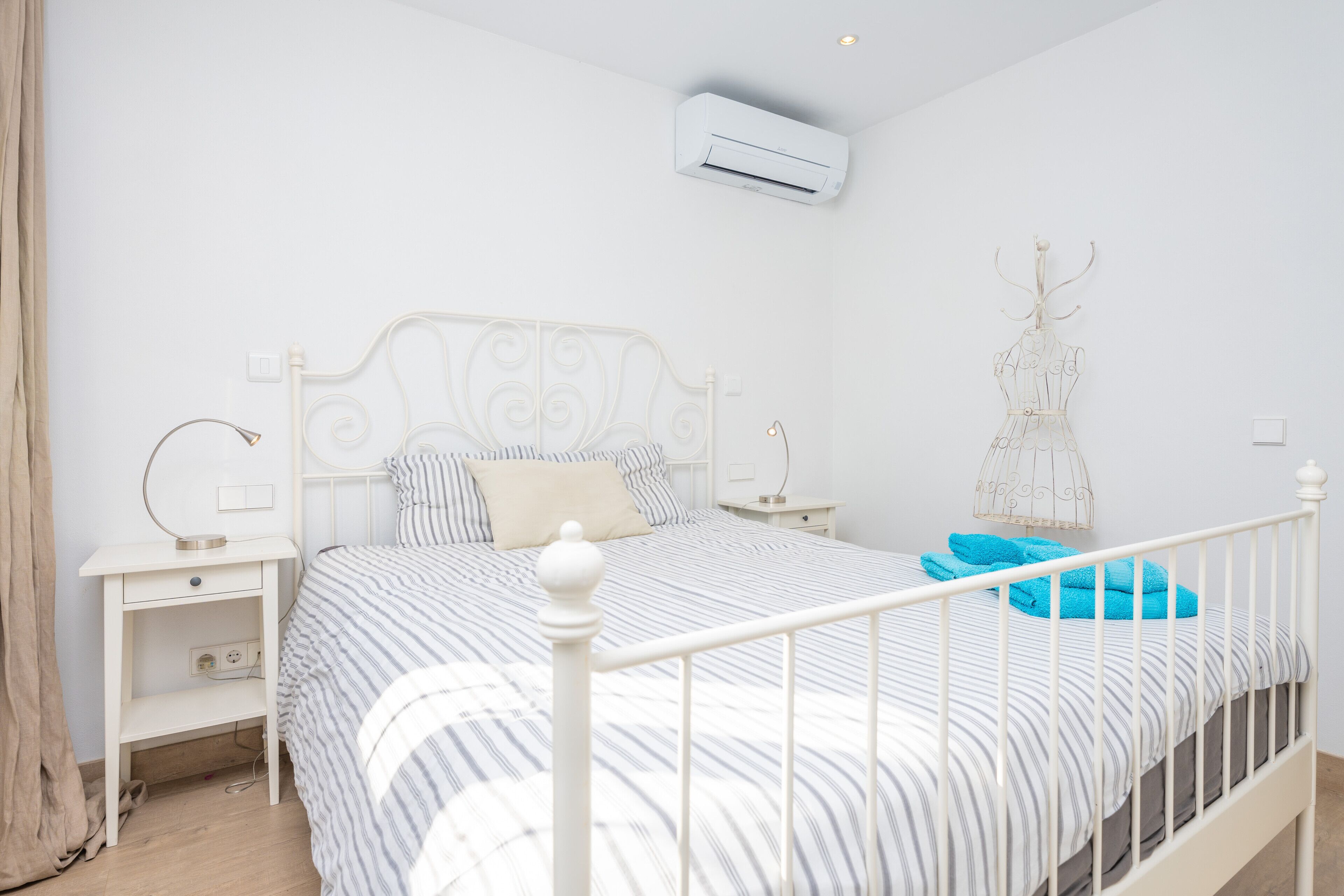 Une chambre à coucher comprenant un lit, des tables de chevet, un climatiseur fixé au mur et un élément décoratif mural.