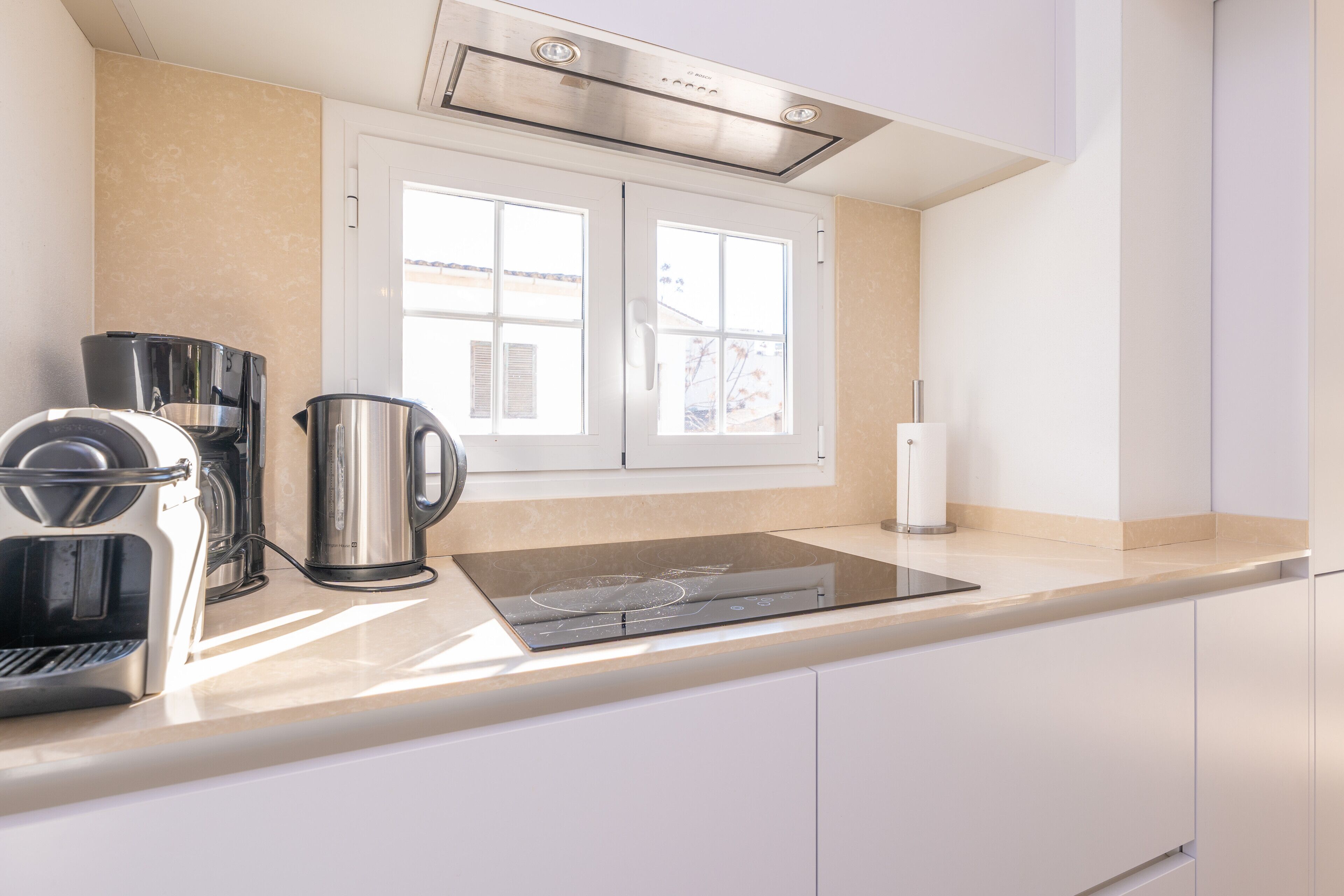 Eine moderne Küche mit Einbauherd, Kaffeemaschine, Wasserkocher und einem Fenster mit Jalousien.