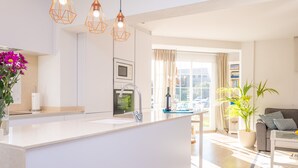 Une cuisine moderne dotée d’un îlot central, d’un coin repas avec une table et des chaises, d’un canapé et d’une grande fenêtre agrémentée de rideaux.