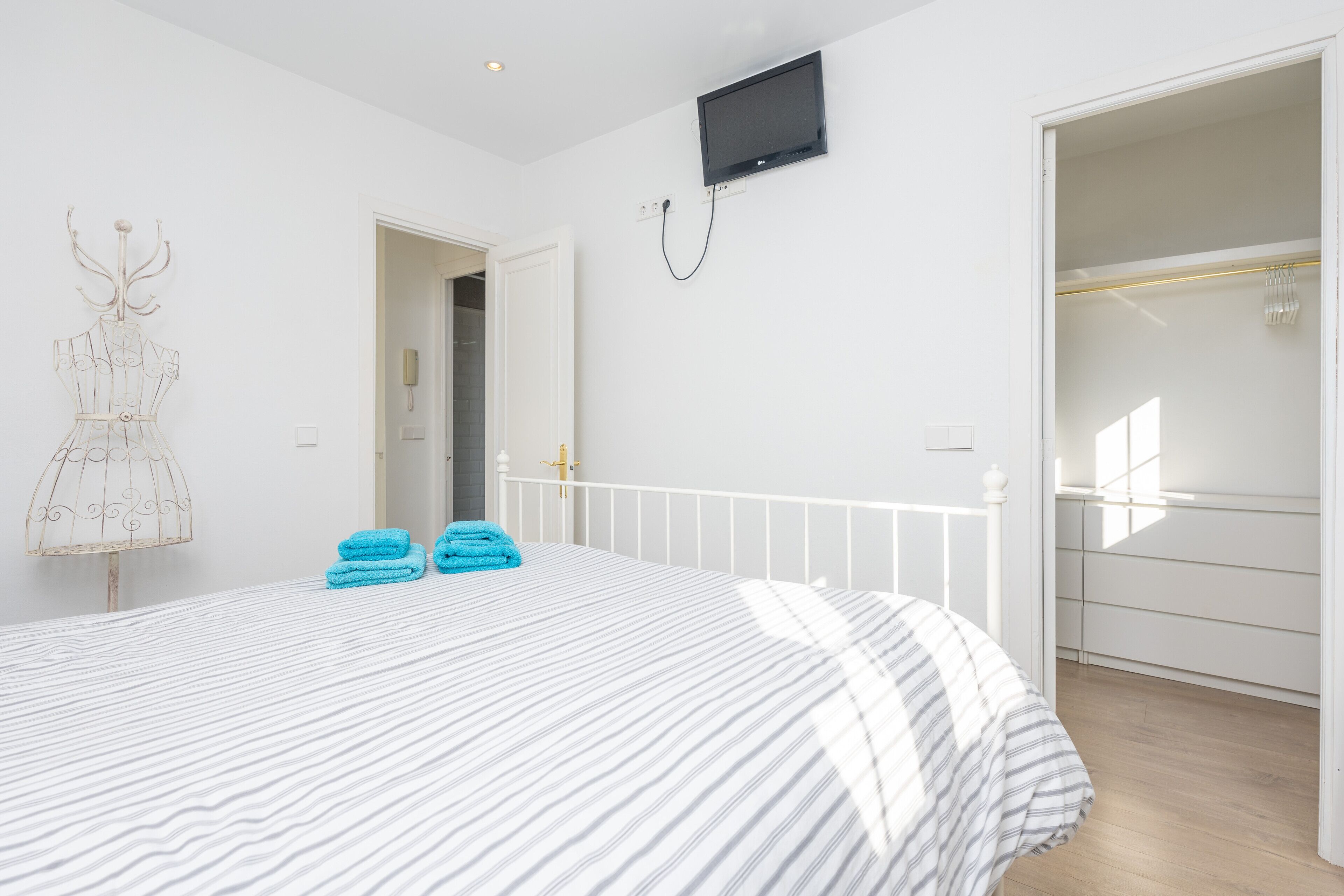 A bedroom with a bed, a TV mounted on the wall, and a door leading to another room.