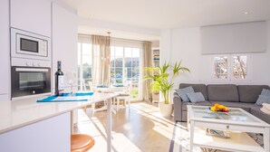 Un appartement moderne comprenant une cuisine, un coin repas et un salon. Il est doté d’une grande fenêtre, d’une plante en pot et d’un canapé avec des coussins.