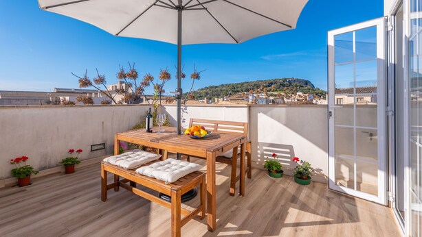 Une terrasse en bois avec une table et des chaises, un grand parasol et des plantes en pot.