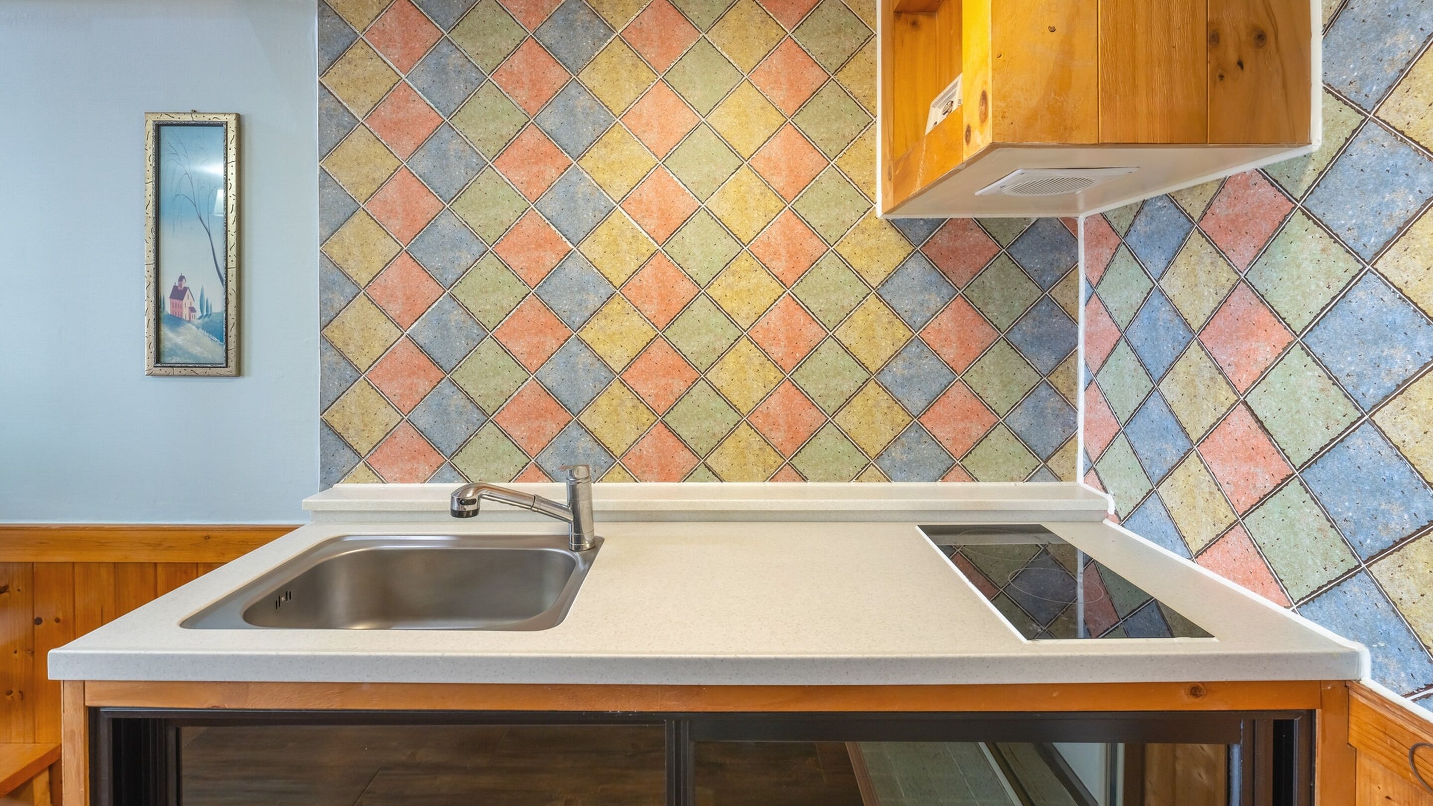 A kitchen with a sink, wooden cabinets, and colorful diamond-patterned tiles on the backsplash.