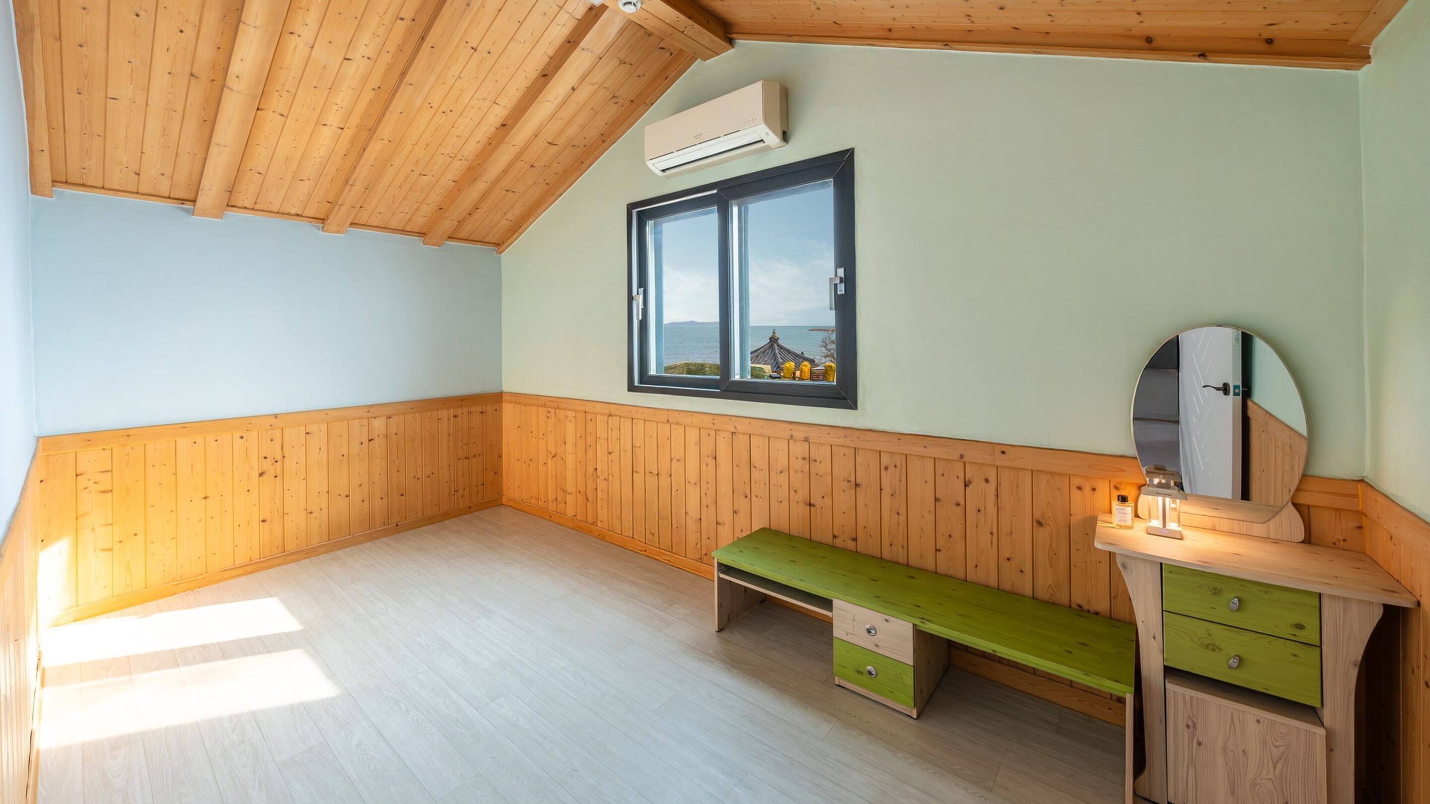 A room with wooden paneling, a window with a view, a bench, and a small desk with drawers.