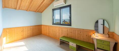 A room with wooden paneling, a window with a view, a bench, and a small desk with drawers.