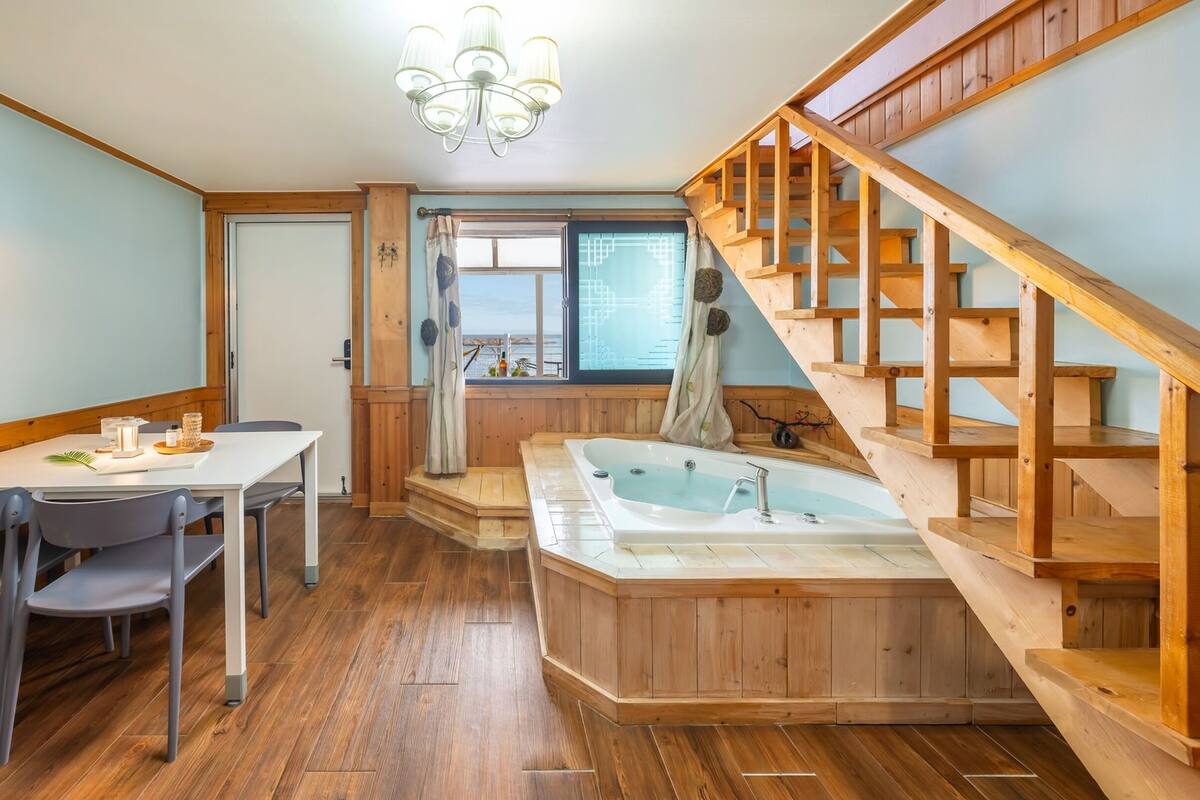 A wooden interior with a dining area, a hot tub, and a staircase.