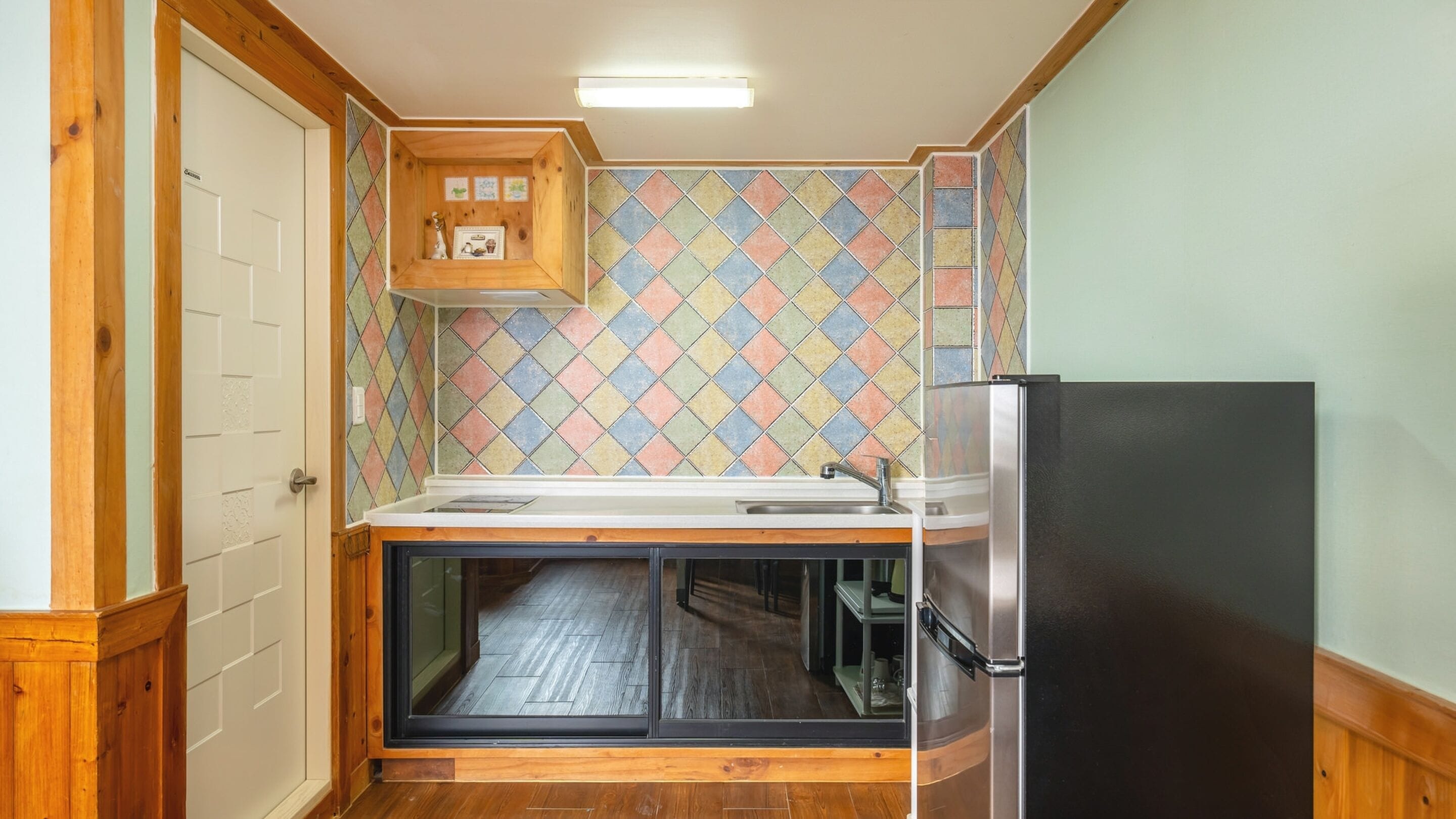 A compact kitchen with a wooden cabinet, a refrigerator, and a tiled backsplash.