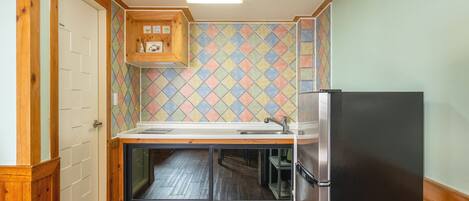 A compact kitchen with a wooden cabinet, a refrigerator, and a tiled backsplash.