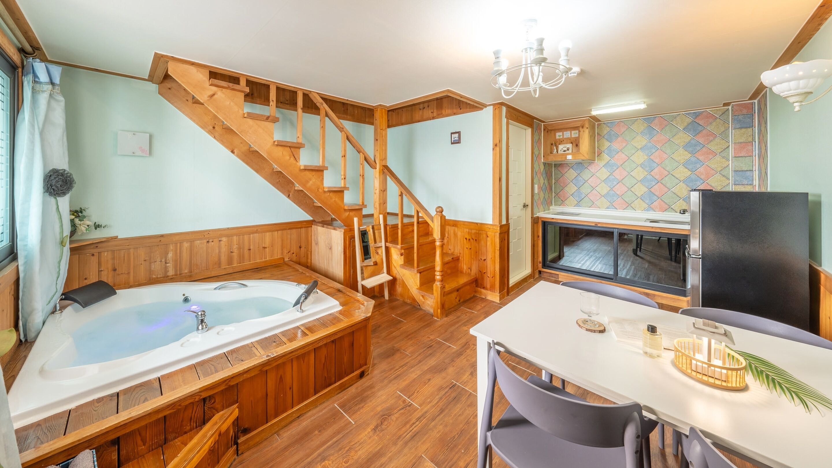 Une pièce chaleureuse avec un escalier en bois, un jacuzzi, un coin repas et une cuisine avec un dosseret carrelé.