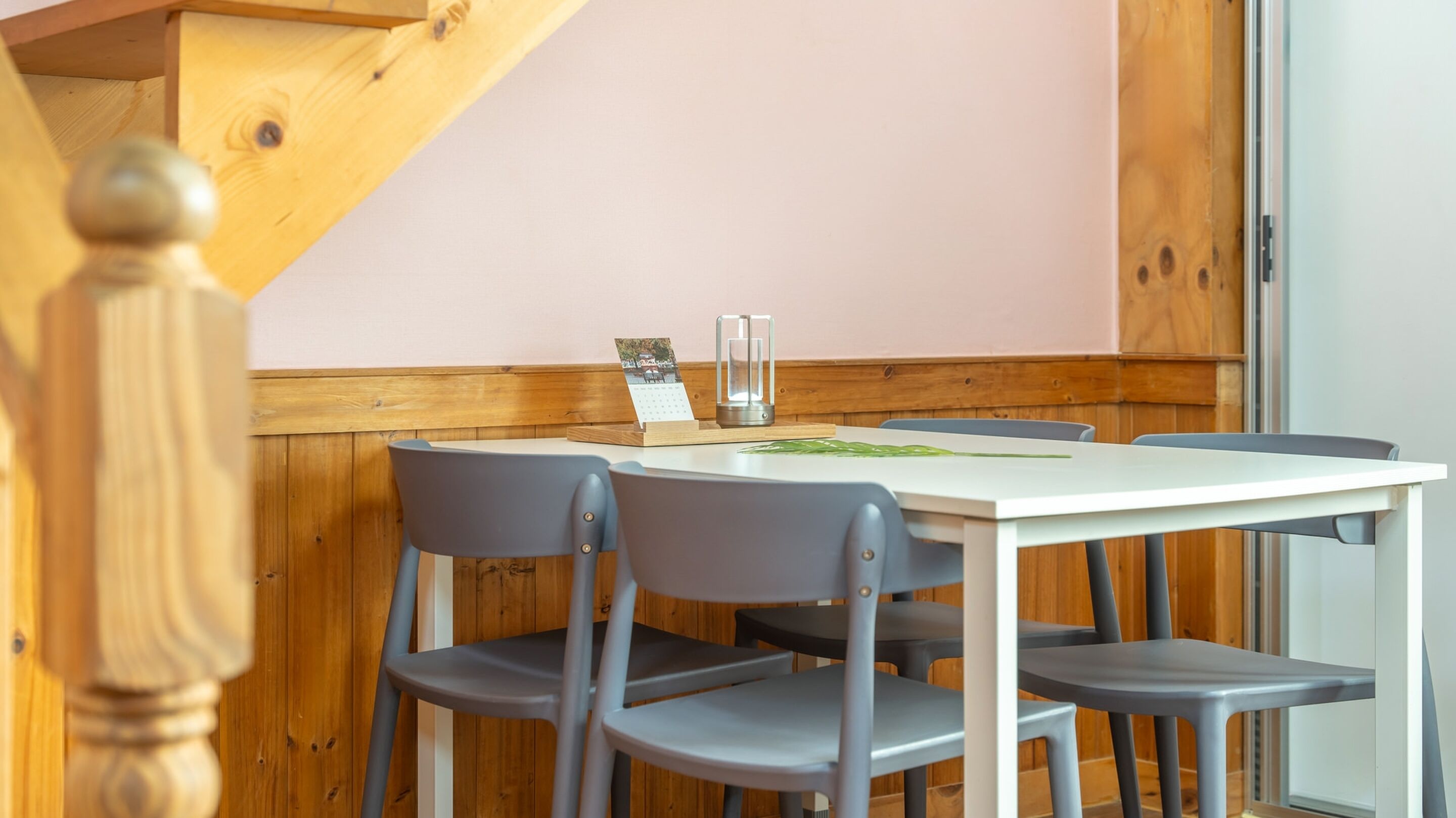 A dining area with a white table, four grey chairs, a wooden bench, and a calendar on the table.