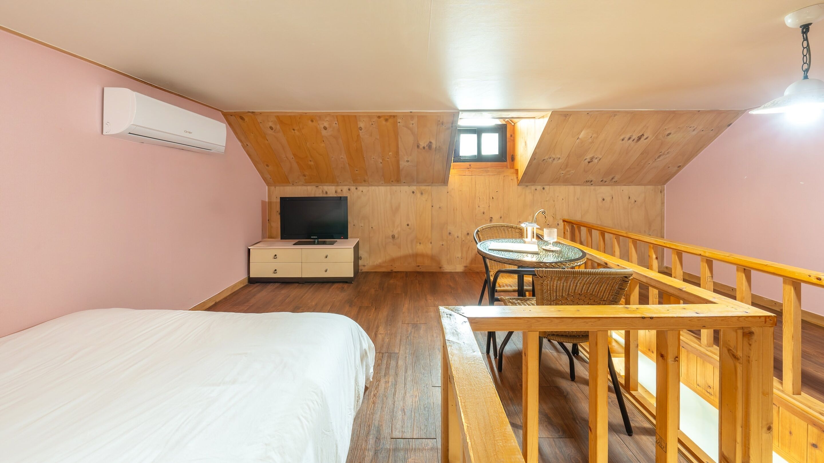 A bedroom with a bed, a dresser, a TV, and a small balcony with a table and chairs.