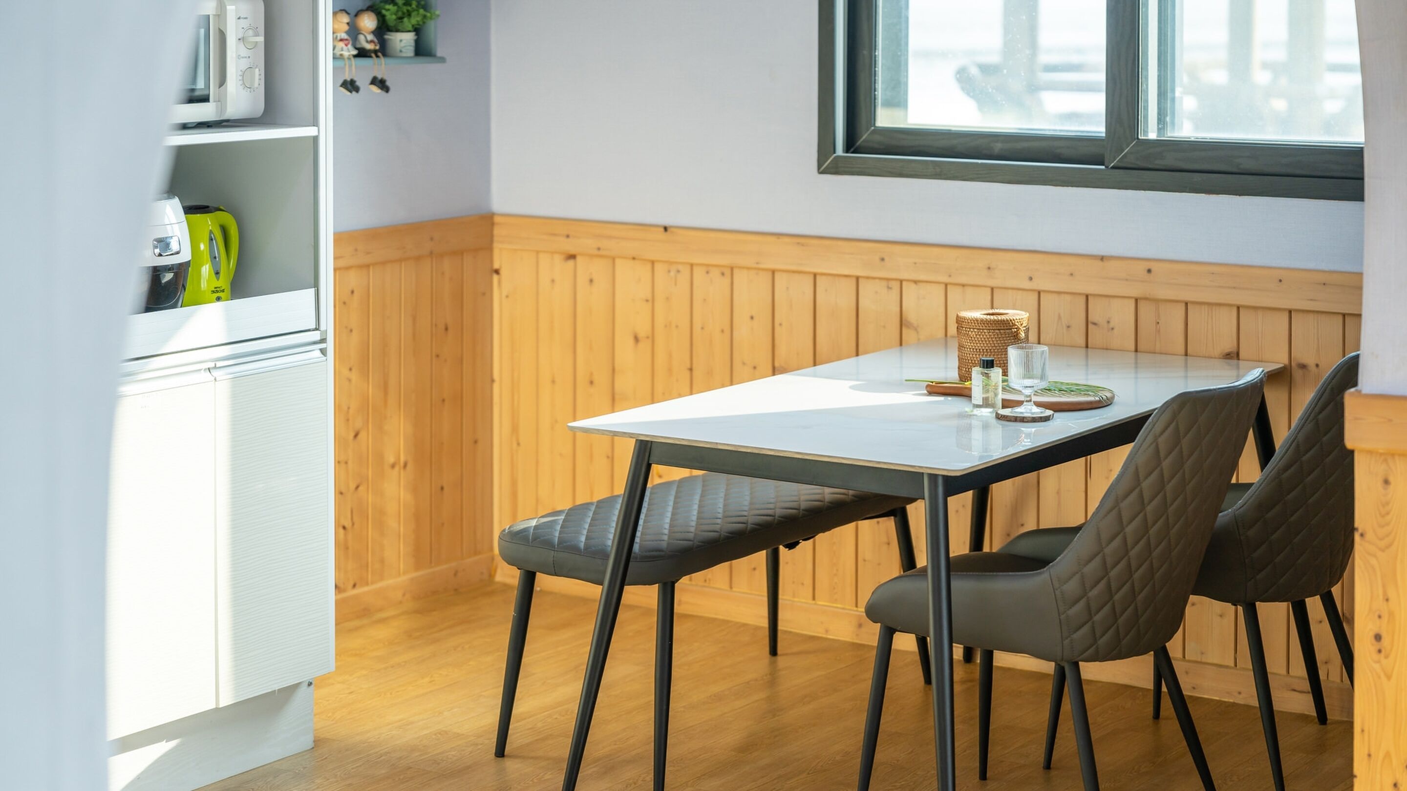 Una cucina compatta con frigorifero bianco, un pensile in legno e una finestra sopra un tavolo con due sedie.