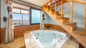 A spa room with a large bathtub, wooden flooring, a window with curtains, and a wooden staircase. - Yeongheungdo Blue Story Pension (Incheon)