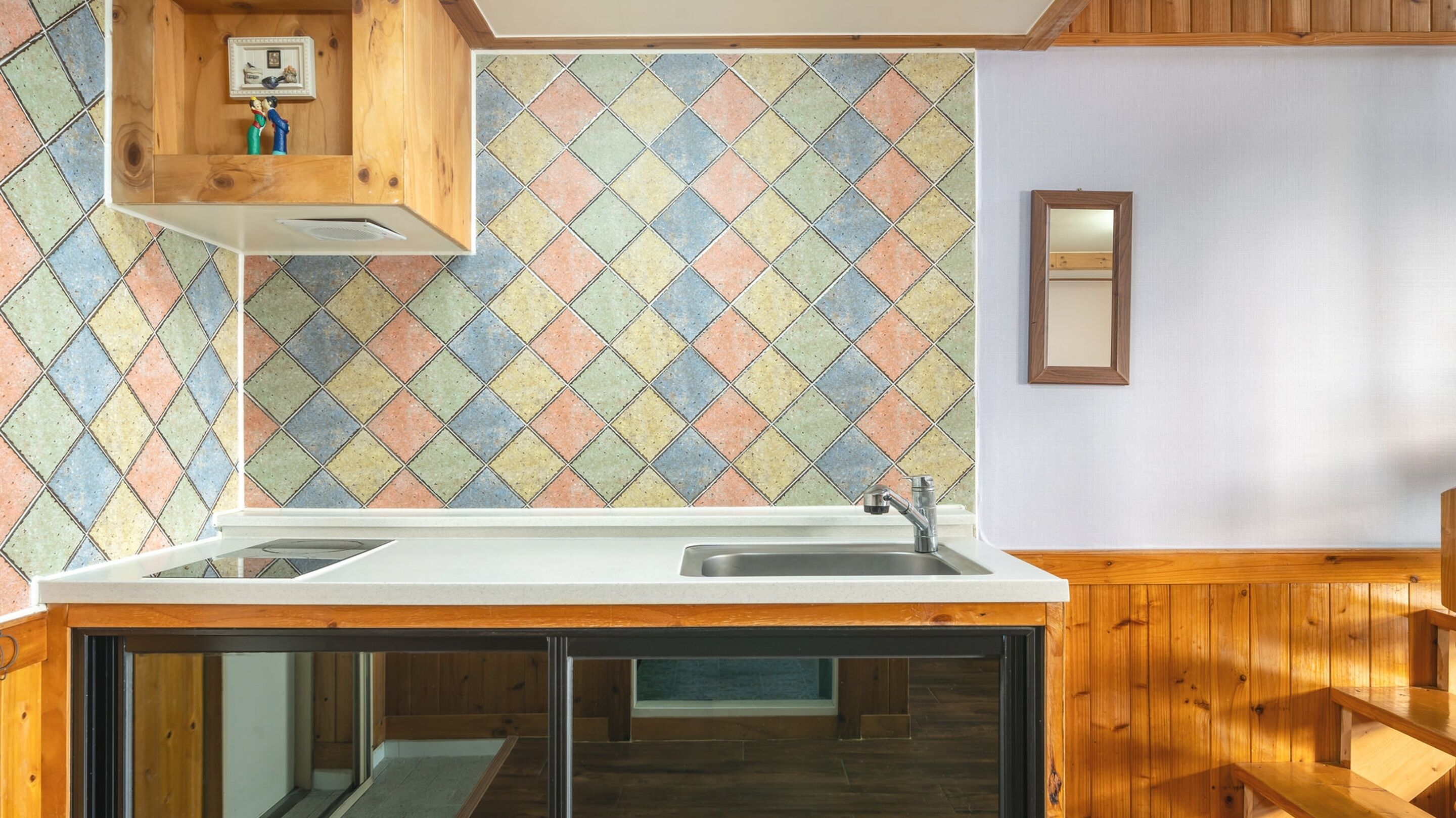 Une cuisine avec un crédence aux motifs géométriques colorés, des armoires en bois et une fenêtre intégrée.