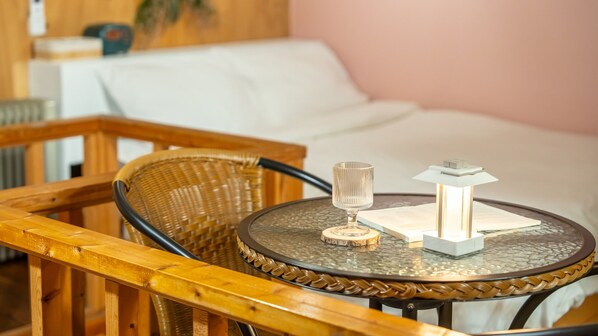 A round glass table with a woven chair, a glass, and a small table lamp in a room with a white bed and a pink wall. - Yeongheungdo Blue Story Pension (Incheon)