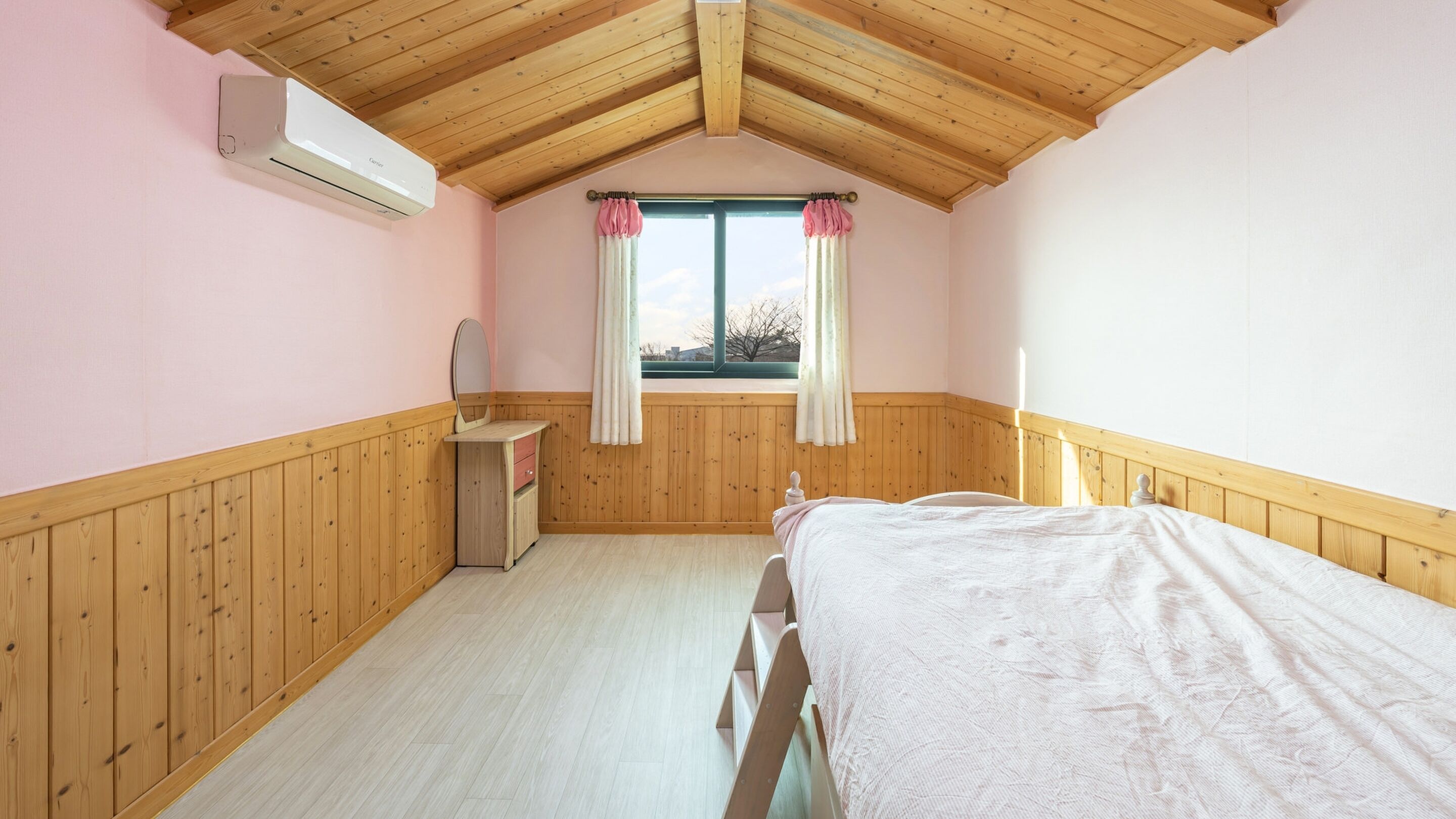 A bedroom with wooden paneling, a bed, a bedside table with a mirror, and a window with curtains.