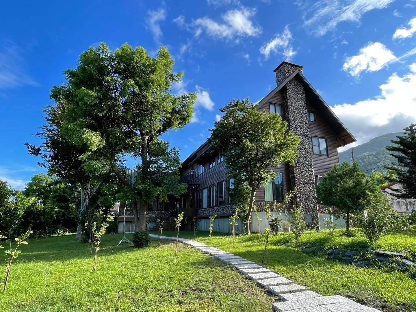 A two-story house with a stone facade and a sloped roof, surrounded by a well-maintained lawn and trees.