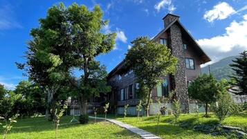 A two-story house with a stone facade and a sloped roof, surrounded by a well-maintained lawn and trees.