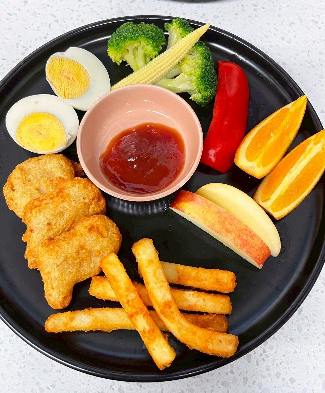 Une assiette de nourriture comprenant du poisson, des frites, des œufs durs et des légumes.