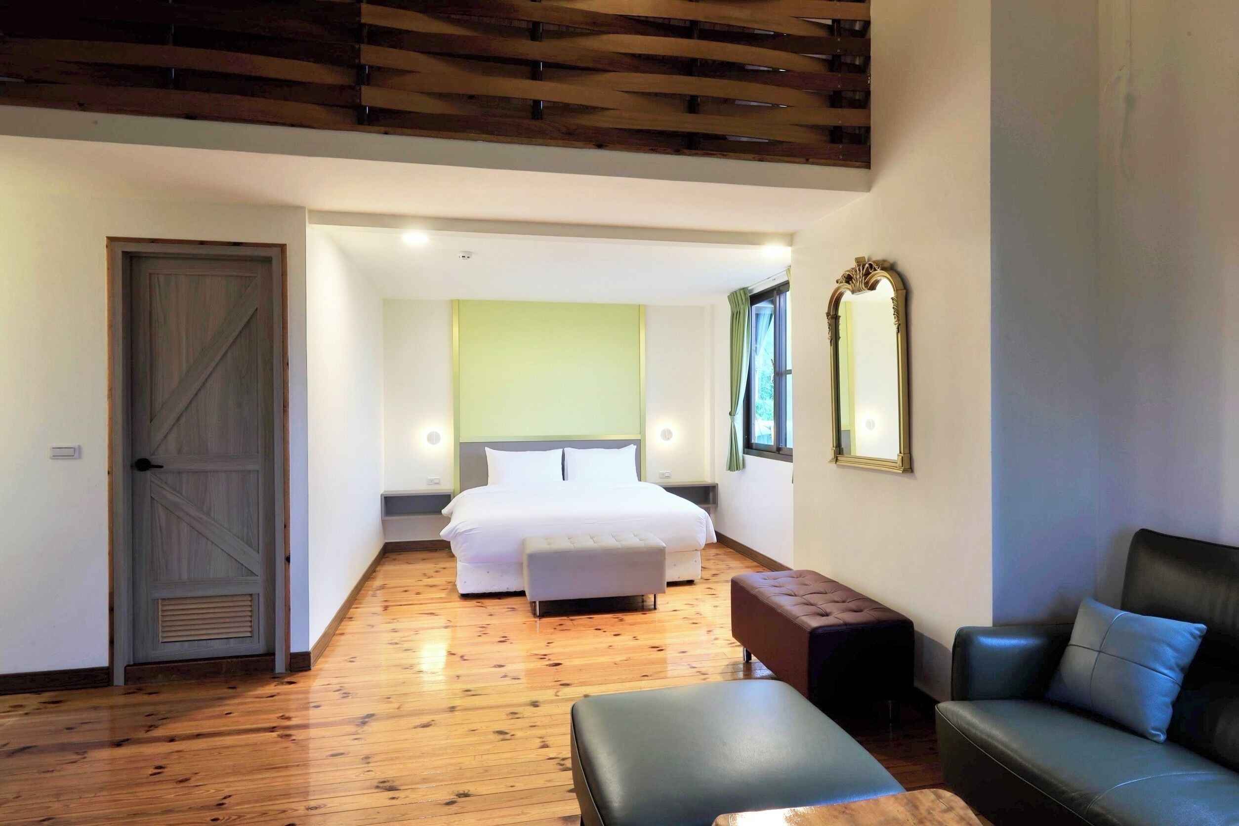 A hotel room with a wooden floor, a bed, a sofa, a small table, and a mirror on the wall.