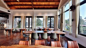 A spacious dining area with wooden tables and chairs, large windows, and a high ceiling with exposed beams. - DF Life Lodge (Luye)