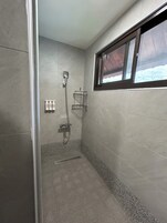 Ducha con ventana, repisa metálica y piso de baldosas.