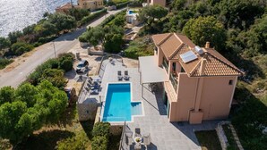 Une villa située sur la côte, dotée d’une piscine, de bâtiments aux toits de tuiles et offrant une vue sur la mer.