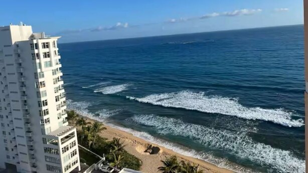 A high-rise building overlooking a beach with waves crashing onto the shore.