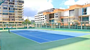 An outdoor tennis court surrounded by multi-story buildings.