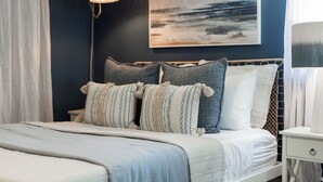 Une chambre à coucher comprenant un lit, une table de chevet, une lampe, un tableau mural et un luminaire suspendu.