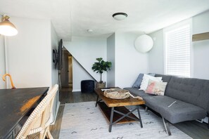 En moderne stue med en sofa, et sofabord, et fjernsyn og en trappe til et andet rum.