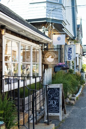 A coastal-themed storefront with a wooden sign, a chalkboard sign, and a white picket fence.