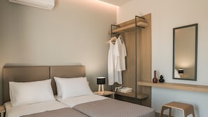 Una cama doble con cabecera, una mesita de noche con lámpara, un estante de madera con espejo y un pequeño taburete.
