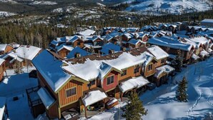 A snow-covered village with wooden cabins and a mountain backdrop. - 8 Mins to Trails | Near Shuttle (Winter Park)