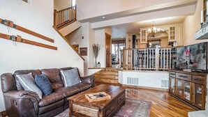 A spacious living room with a brown leather sofa, wooden coffee table, and a view of the kitchen and dining area. - 8 Mins to Trails | Near Shuttle (Winter Park)