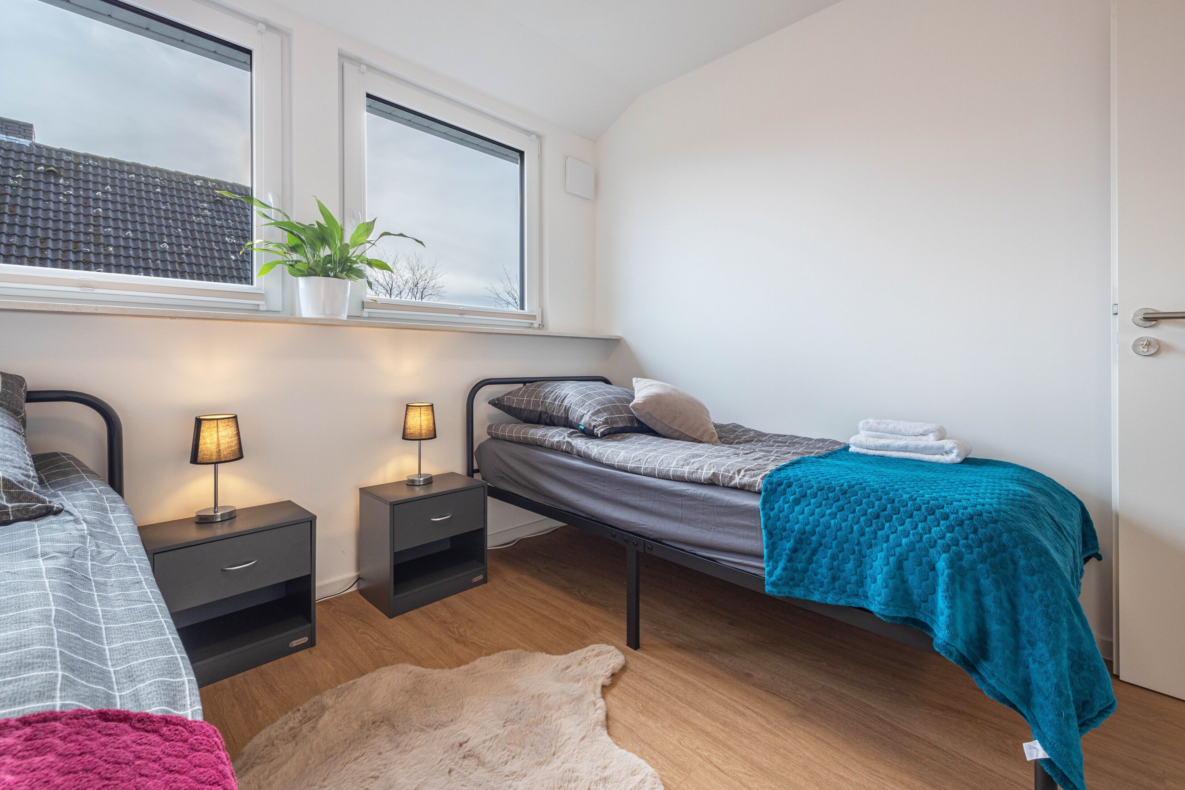 A bedroom with a bed, bedside tables, a window, a plant, and a rug.