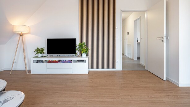 Een moderne woonkamer met een flatscreen-tv, een witte tv-meubel, een vloerlamp en een wand van houten latten.