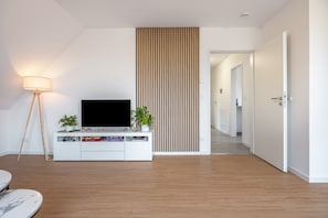 A modern living room with a flat-screen TV, a white entertainment unit, a floor lamp, and a wooden slat wall. - Apartment 'Kroge' with Balcony and Wi-Fi (Uelzen)