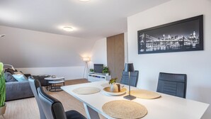 Een moderne woonkamer met een eethoek, een bank, een salontafel, een lamp en een stadsgezichtschilderij aan de muur.
